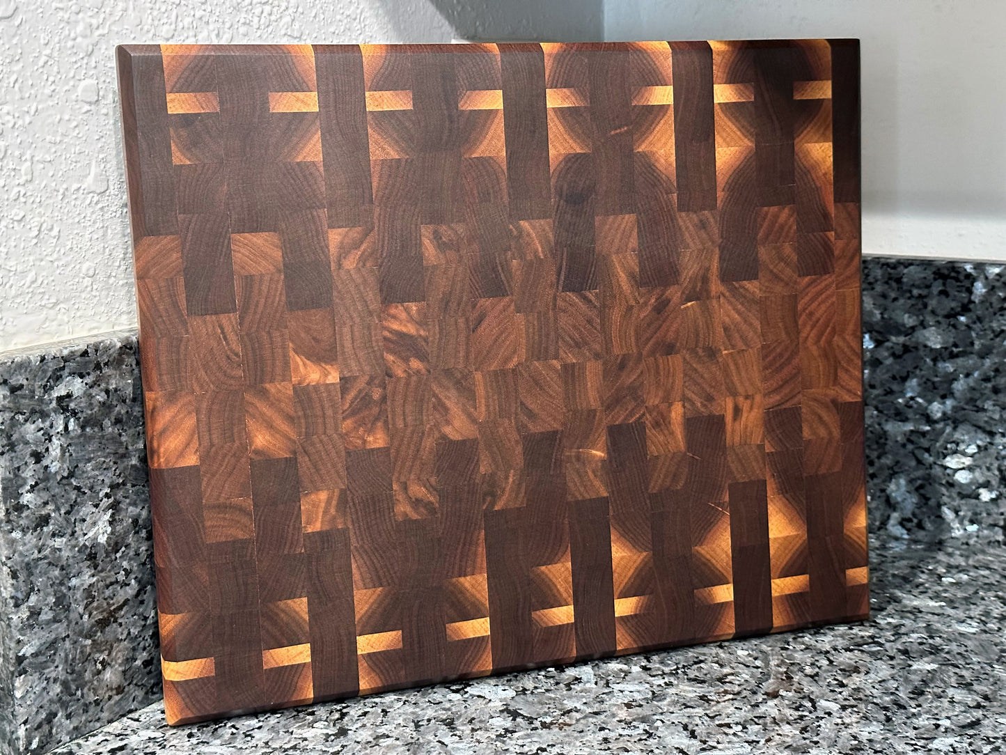 Crafted from the finest hardwoods in North America, this mosaic inspired end grain cutting board features rich black walnut. Chamfered edges give a modern twist to the classic cutting board styling. Hard rubber feet gives the chef a stable worksurface along with providing air circulation under the board, allowing it to dry after washing. Board dimensions: 14.75"L x 12"W x 1.25"H. As a handcrafted product, please allow for approximately 1/4" variation in dimensions.