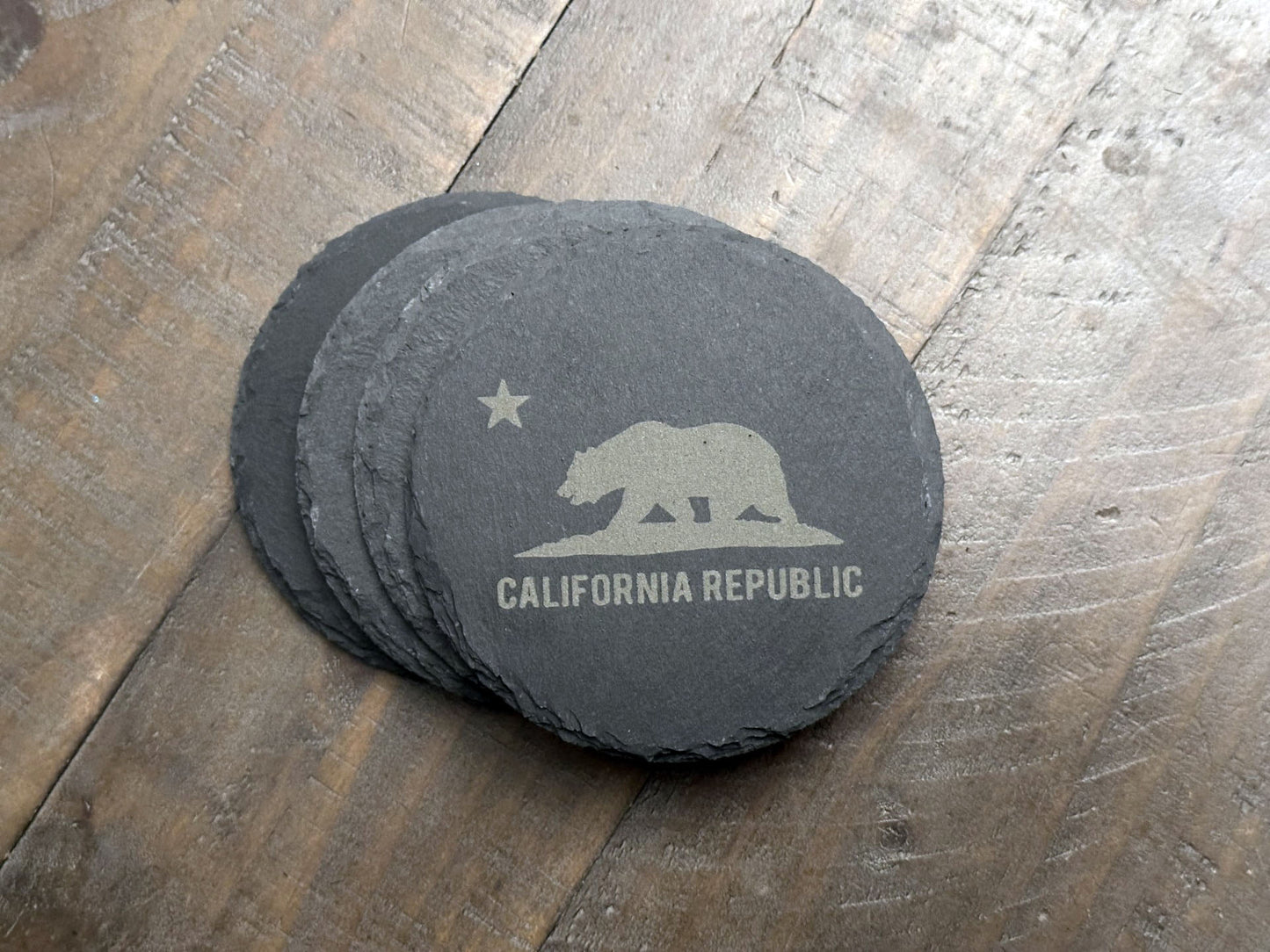 These California themed slate coasters are a real "bear" necessity to show off some state pride. Laser engraved with either the state's outline, lone star, and a grizzly bear or the California flag, they’re a bold way to keep your drinks in check. Made from durable slate, these coasters are both functional and stylish, making them a perfect addition to any home or as a gift for lovers of the Golden State.
