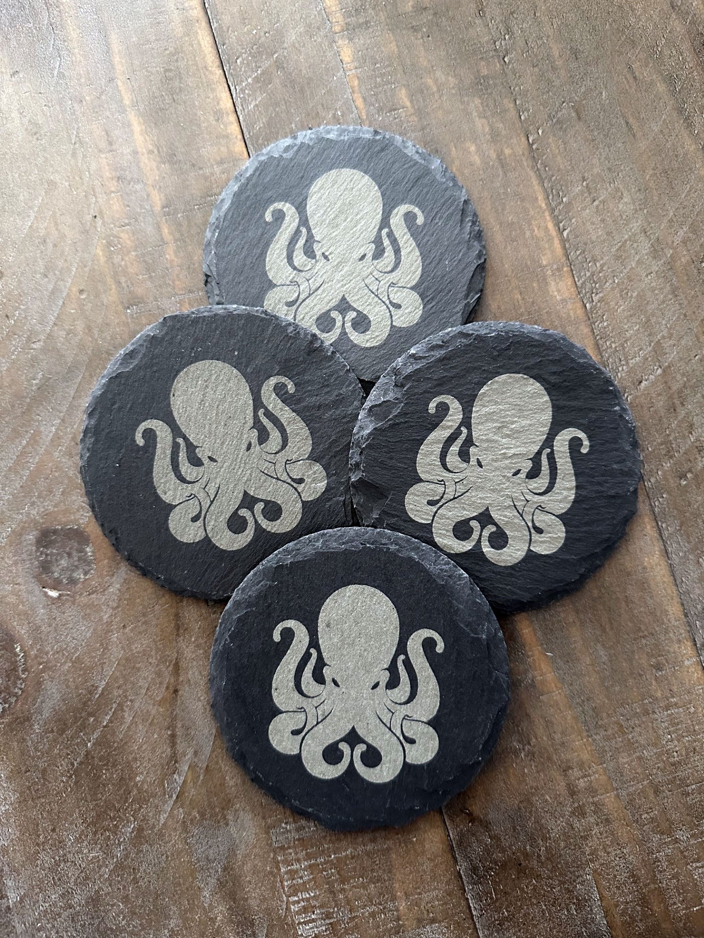 How do you make an octopus laugh? Ten-tickles! Enjoy a beverage while protecting your tabletops with these octopus themed slate coasters! The images are laser engraved onto each slate coaster and are permanent. They won't fade or wash off! Grab a set for that perfect groomsman or house warming gift. These slate coasters will also be right at home in any man cave or she shed. Makes a great holiday present or stocking stuffer, too! Coasters include padded feet attached.