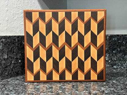 Crafted from the finest hardwoods in North America, this chevron pattern inspired end grain cutting board features rich black walnut and maple framed with cherry accents. Chamfered edges give a modern twist to the classic cutting board styling. Hard rubber feet gives the chef a stable worksurface along with providing air circulation under the board, allowing it to dry after washing. Board dimensions: 12"L x 10.5"W x 1"H.