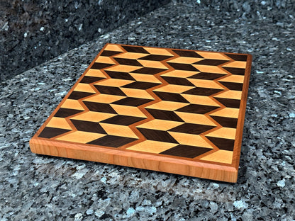 Crafted from the finest hardwoods in North America, this chevron pattern inspired end grain cutting board features rich black walnut and maple framed with cherry accents.  Chamfered edges give a modern twist to the classic cutting board styling. Hard rubber feet gives the chef a stable worksurface along with providing air circulation under the board, allowing it to dry after washing.  Board dimensions:  12"L x 10.5"W x 1"H. 