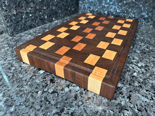 Crafted from the finest hardwoods in North America, this end grain butcher block features rich black walnut with cherry and maple accents.  Chamfered edges and finger grooves give a modern twist to the classic butcher block styling. Hard rubber feet gives the chef a stable worksurface along with providing air circulation under the block, allowing it to dry after washing.  Board dimensions:  18"L x 12"W x 1.75"H.  As a handcrafted product, please allow for approximately 1/4" variation in dimensions.