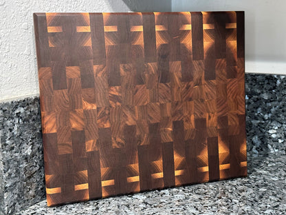 Crafted from the finest hardwoods in North America, this mosaic inspired end grain cutting board features rich black walnut.  Chamfered edges give a modern twist to the classic cutting board styling. Hard rubber feet gives the chef a stable worksurface along with providing air circulation under the board, allowing it to dry after washing.  Board dimensions:  14.75"L x 12"W x 1.25"H.  As a handcrafted product, please allow for approximately 1/4" variation in dimensions.