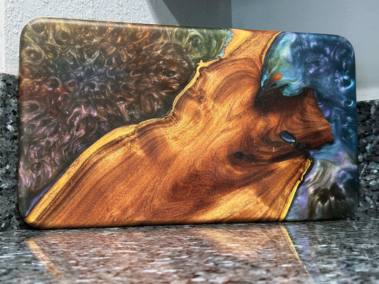 The natural beauty of this live edge mesquite serving board is accented with a blast of color.  Dark blues and purples swirl together like a galactic nebula while a bubbling sea of color hypnotizes.   Food safe epoxy resin was used to create this design. Using knives or other sharp utensils on the epoxy resin surface may damage it and is not recommended.  Board dimensions:  17"L x 9.75"W x 0.75"H.  As a handcrafted product, please allow for approximately 1/4" variation in dimensions.