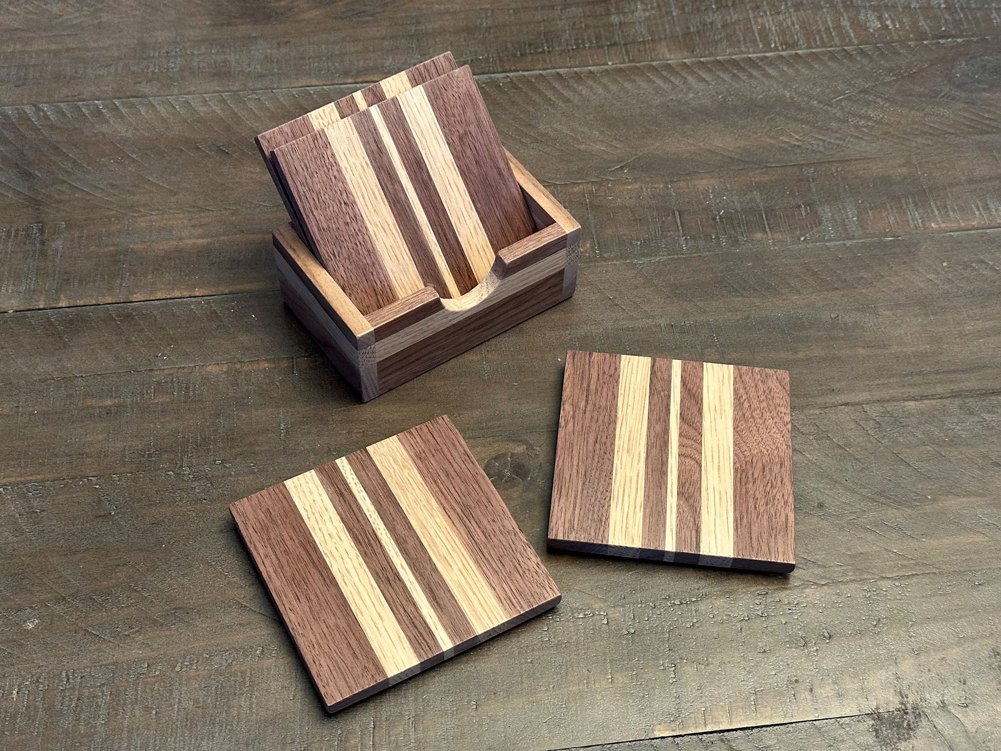 Enjoy a beverage while protecting your tabletops with these walnut and white oak hardwood coasters.  Available in a set of 4 coasters and includes a custom holder.  Each coaster is coated in polyurethane for water resistance and they have felt footpads to protect your surfaces.  As a handmade wood product, there will be slight variation between the product you receive and the listed images.